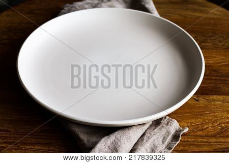 Single Empty Light Grey Plate Over Grey Fabric Napking And Wooden Board