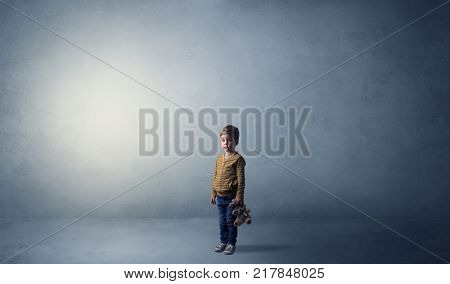 Little waggish kid staying alone in a big empty room with his plush