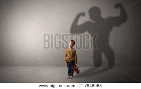 Little waggish boy in an empty room with musclemen shadow behind
