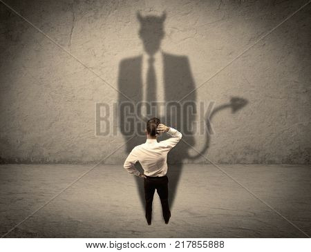 An experienced tricky businessman in suit looking at his devil desguise shadow reflected on the wall concept