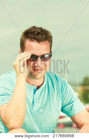 Fashion details and accessories concept. Portrait of handsome guy during summertime wearing blue tshirt and sunglasses.