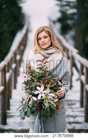 Beautiful Young Girl Stands In Winter With A Bouquet Of Flowers In Her Hands