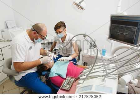 Process of preparing and installing dental ceramic crown. Male professional dentist and female assistant helps to treat the teeth of woman patient in clinic light office with modern tools equipment