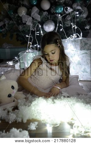 Portrait of little girl wait a New Year With her favorite toy. Cute girl surrounded by Christmas lighting