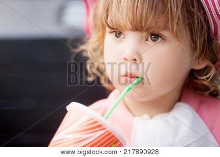 Adorable little girl drinking from glass with straw wearing straw hat summer vaccation.