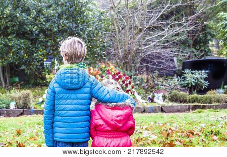 Little brother and sister standing at the grave of their parents in the graveyard