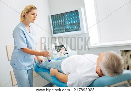 Medical assistant. Pleasant nice skillful woman standing near the patient and using an ultrasound device while doing medical checkup