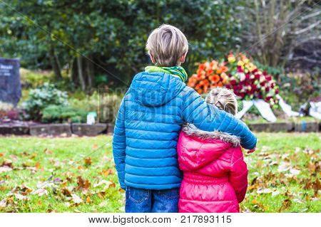 Little brother and sister standing at the grave of their parents in the graveyard