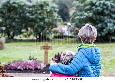 Little brother and sister standing at the grave of their parents in the graveyard