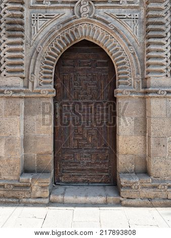 Cairo, Egypt - December 2, 2017: Grunge wooden ornate aged vaulted arched door on exterior decorated stone bricks wall at Manial Palace of prince Mohamed Ali Medieval Cairo