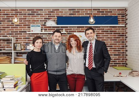 Portrait Of Office Staff Standing In Office. Team is looking at camera and smiling while standing in thei working space.