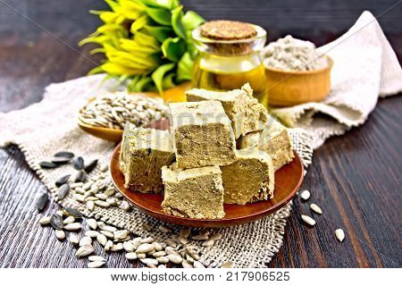 Eastern sweet halva sunflower in a plate, sunflower seeds, oil, flour and flower on a sacking on a background of a dark wooden board