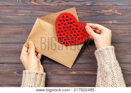 Top view. Hand of girl writing love letter on Saint Valentines Day. Handmade postcard with red heart shaped figure. 14 February holiday celebration. Valentine day concept with copyspace.