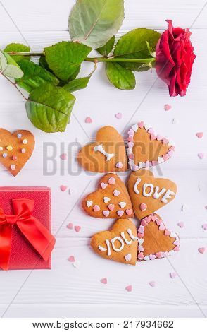 Homemade cookies in shape of heart with I Love you words as gift for lover on Valentine's day. White wooden table with greeting card rose and decor. Festive gift concept. Selective focus. Copy space.