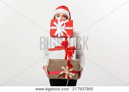 Business Concept - Beautiful young caucasian business woman with santa hat hiding behide a lot of christmas gift boxes with copy space on side.