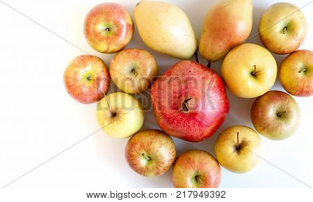 Group of colorful ripe fruits in form of heart: apples, pears and one big granate on white background with copy space.