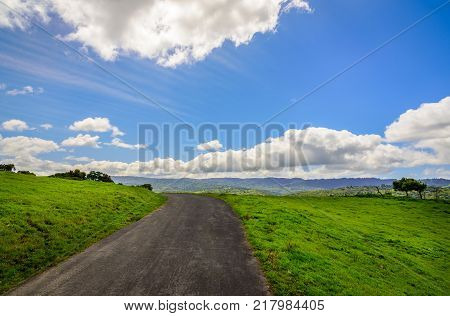 Green grass hill and the road on the top. Blue sky and white clouds