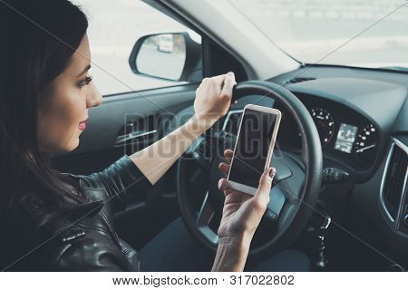 Young Woman Looking To Her Smartphone While Driving Car At Front Window Background. Distracted Femal
