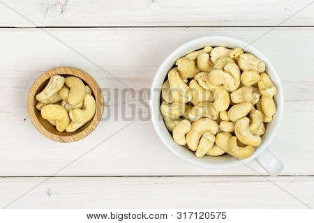 Lot Of Whole Unsalted Beige Cashew In Tiny Wooden Bowl Flatlay On White Wood