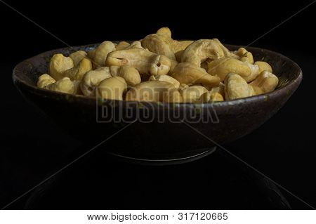 Lot Of Whole Unsalted Beige Cashew In Dark Ceramic Bowl Isolated On Black Glass