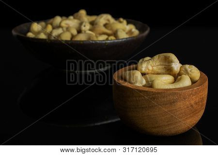 Lot Of Whole Unsalted Beige Cashew In Tiny Wooden Bowl In Dark Ceramic Bowl Isolated On Black Glass