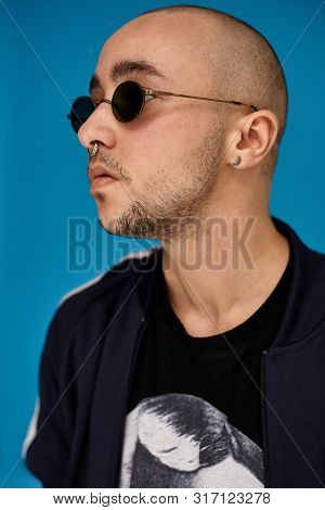 Studio Shot Of A Young Tattoed Bald Man Posing Against A Blue Background. 90s Style.
