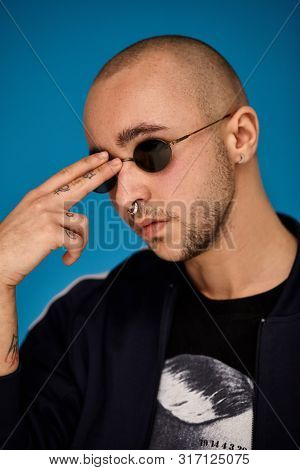 Studio Shot Of A Young Tattoed Bald Man Posing Against A Blue Background. 90s Style.