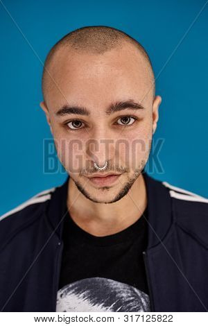 Studio Shot Of A Young Tattoed Bald Man Posing Against A Blue Background. 90s Style.