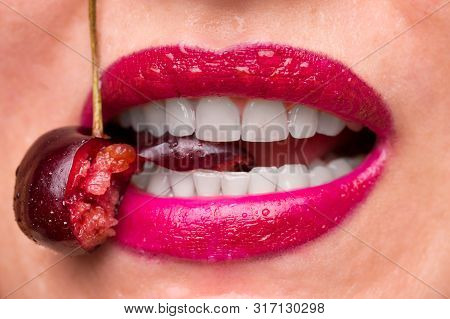 Red Lipstick On Lips And A Cherry With Water Droplets. The Girl Is Eating Cherry. The Flesh Of Bitte