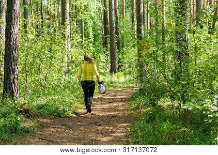 Woman With Garbage Bag Runs Along A Forest Trail During Plogging