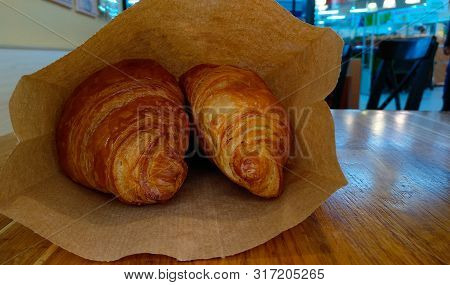 Two Lush Croissants For Breakfast In A Bag With Themselves Lie On A Wooden Table