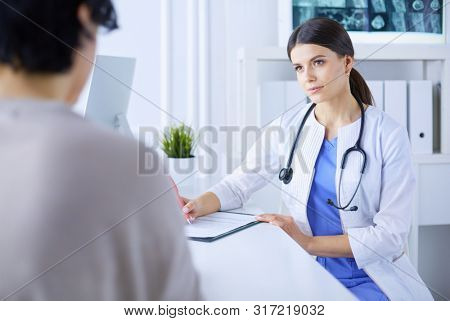 Doctor and patient discussing medical problems in a hospital consulting room. Doc filling in a patient's form