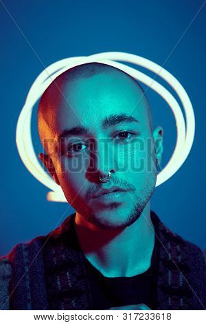 Studio Shot Of A Young Tattoed Bald Man Posing Against A Blue Background. 90s Style.