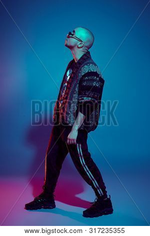 Studio Shot Of A Young Tattoed Bald Man Posing Against A Colorful Background. 90s Style.