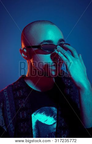 Studio Shot Of A Young Tattoed Bald Man Posing Against A Blue Background. 90s Style.