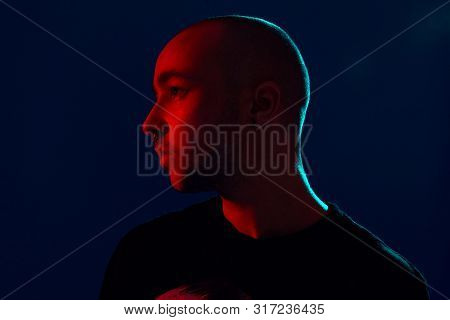 Studio Shot Of A Young Tattoed Bald Man Posing Against A Blue Background. 90s Style.