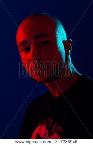 Studio Shot Of A Young Tattoed Bald Man Posing Against A Blue Background. 90s Style.