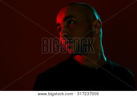 Studio Shot Of A Young Tattoed Bald Man Posing Against A Red Background. 90s Style.