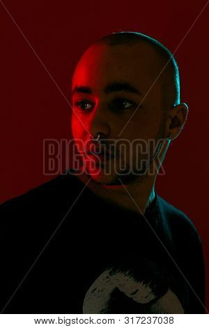 Studio Shot Of A Young Tattoed Bald Man Posing Against A Red Background. 90s Style.
