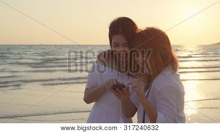 Young Asian Lesbian Couple Using Smart Phone Near Beach. Beautiful Women Lgbt Couple Happy Relax Enj