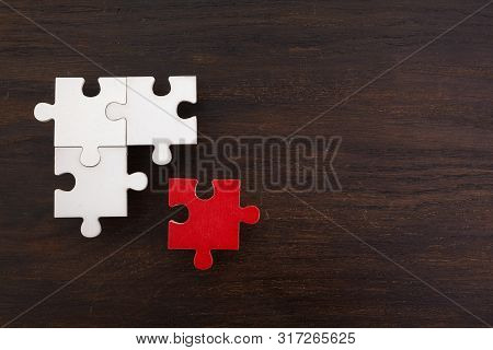 Three Onnected Jigsaw Puzzle Pieces And One Red On Dark Wooden Background. Finding The Right Solutio