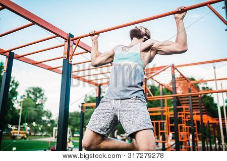 Strong Athlete Doing Pull-up On Horizontal Bar. Muscular Man Doing Pull Ups On Horizontal Bar In Par