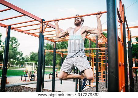 Strong Athlete Doing Pull-up On Horizontal Bar. Muscular Man Doing Pull Ups On Horizontal Bar In Par