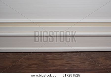 Matte Wall, White Baseboard And Tiles Immitating Hardwood Flooring
