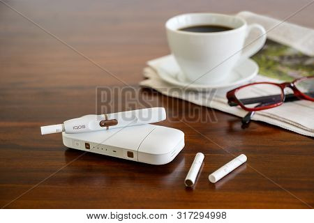 Rieps, Germany, August 15, 2019: Iqos Heating Tobacco System, Coffee Cup And Newspaper On A Brown Ta