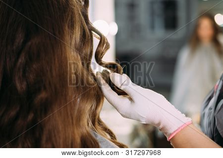 The Hairdresser Makes Curls To The Client, The Female Hand Holds Hair. Beauty Salon, Training L