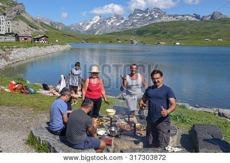 Group Of Happy People Frying Meet On Barbeque Grill At Melchsee-frutt On The Swiss Alps