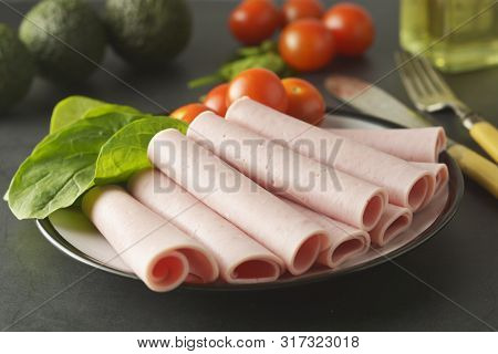Thin Slices Of Ham Rolled On Plate With Fresh Vegetables, Dark Background. Breakfast Food, Ingredien