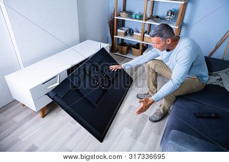 Man Sitting On Sofa In Front Fallen Television With Broken Screen