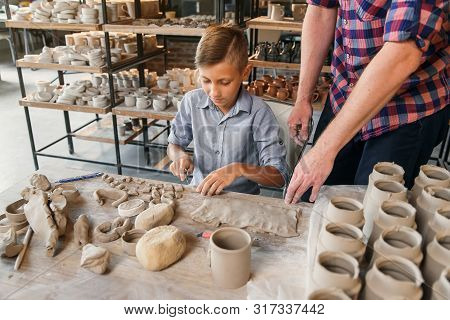 Middle Age Caucasian Father Teaching Little Son How To Work With Clay On Potters Wheel.